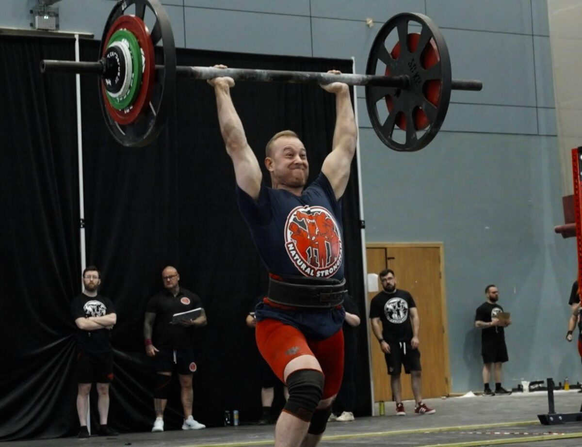 Vegan strength athlete lifting a barbell overhead in competition